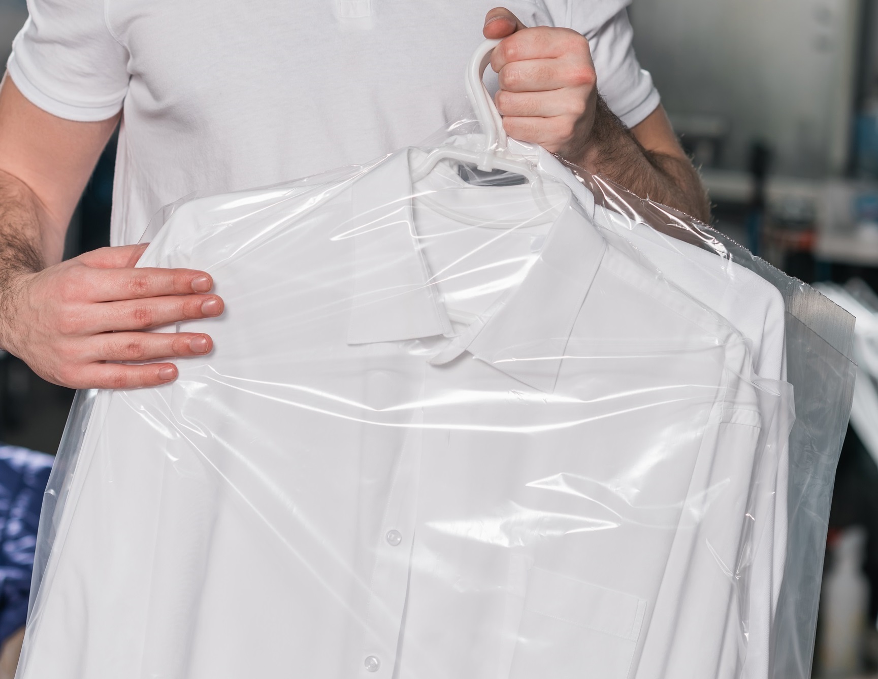 Person holding a white dress shirt covered in plastic, likely from a dry cleaning service. Experience the convenience of Laundry Pick up and Delivery in New York.